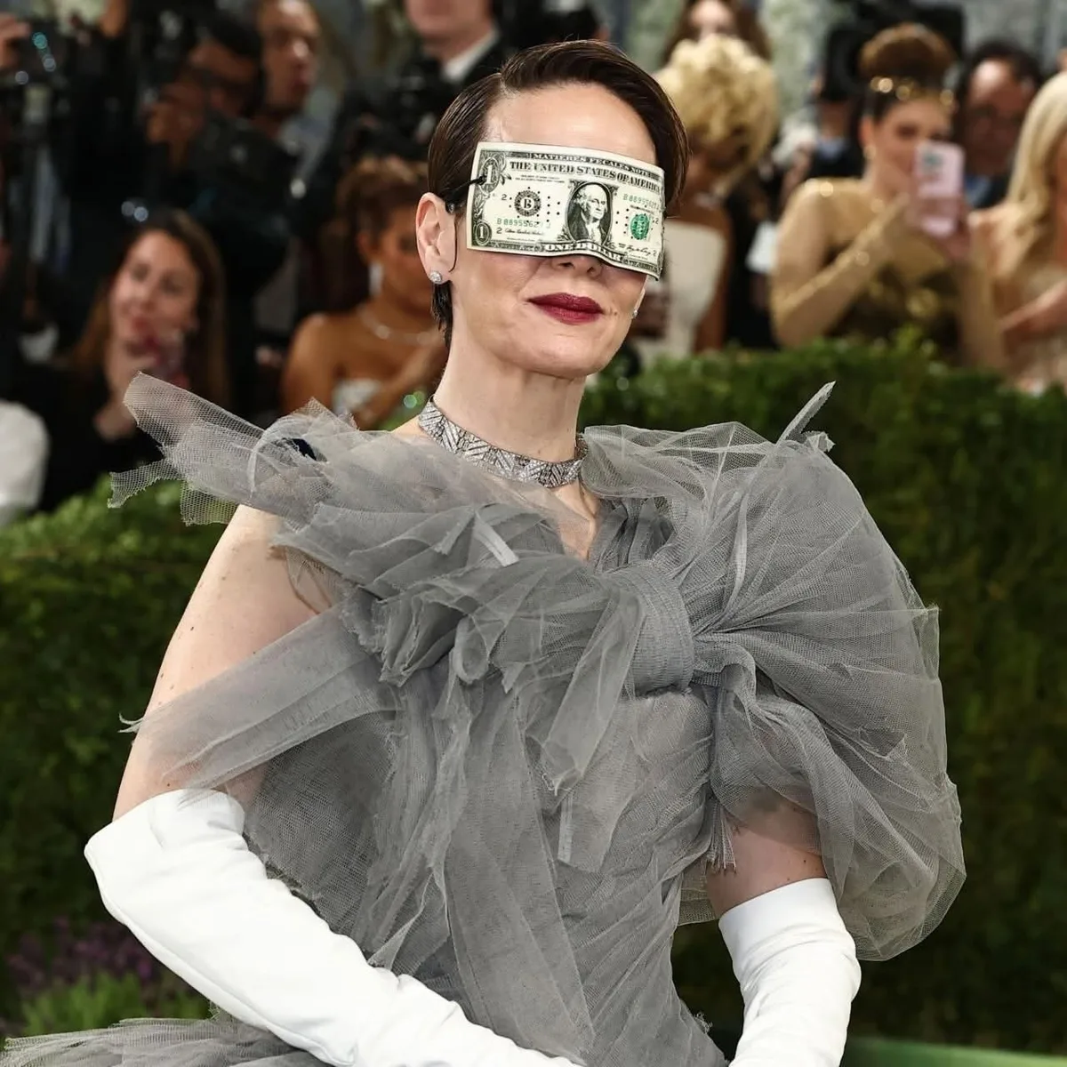 A Met Gala attendee with a one-dollar bill draped across her eyes — the night's most honest accessory.